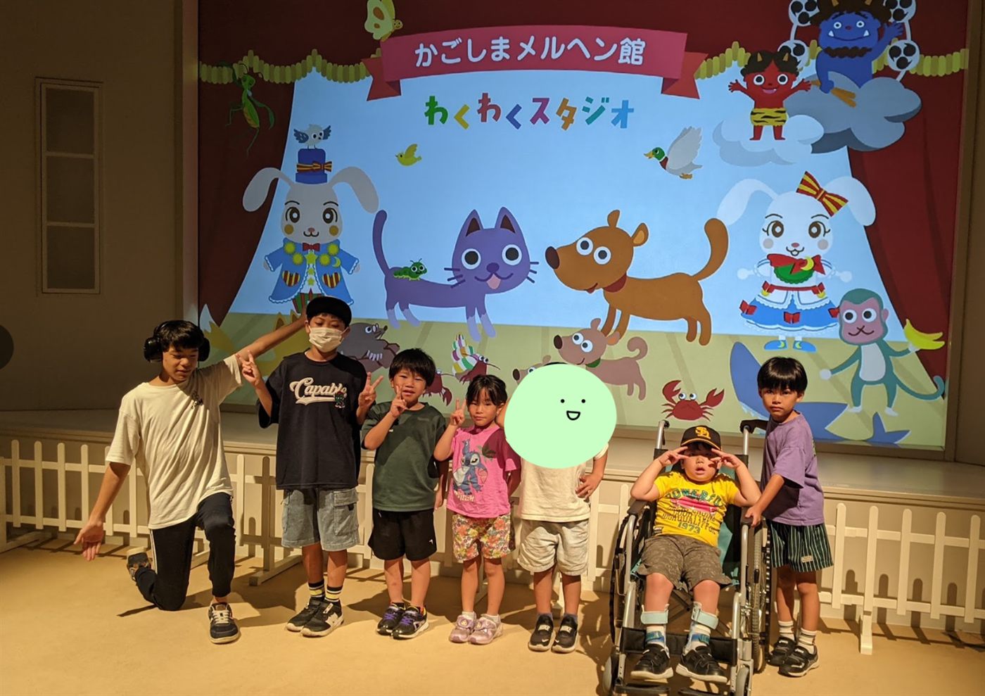 かごしまメルヘン館わくわくスタジオのステージで記念撮影をする子どもたちとスタッフ