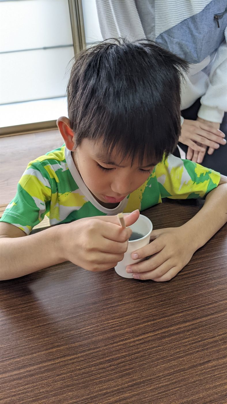紙コップの中の材料を割り箸で混ぜる男の子。スライム作りに集中している様子