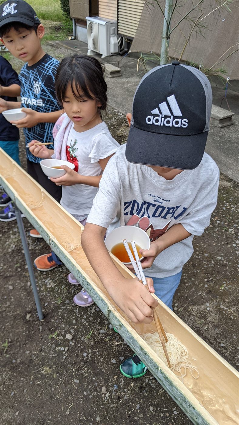 竹の樋を流れてくるそうめんを、おわんを持ちながらお箸でつかまえる男の子