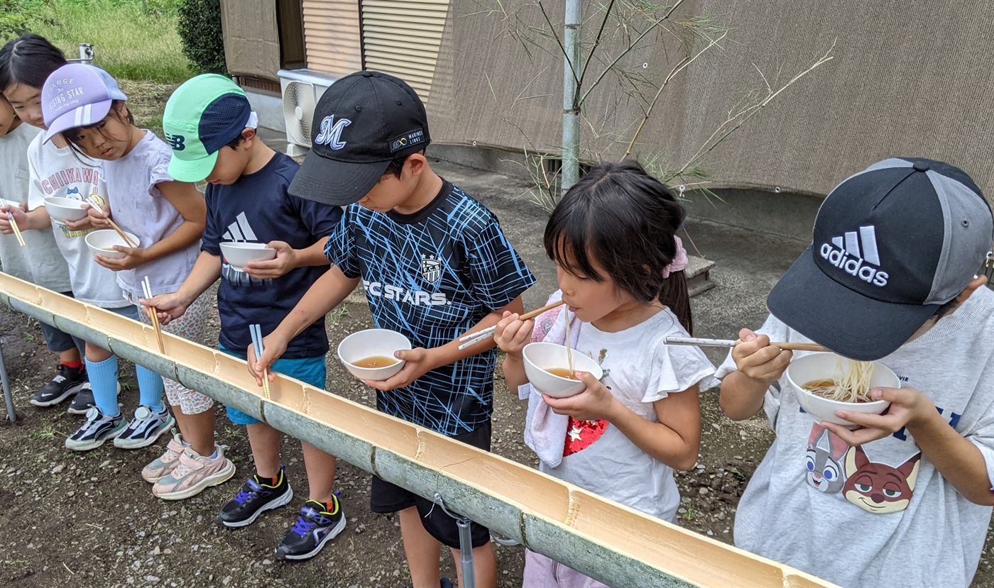竹の樋に沿って並び、それぞれおわんとお箸を持ってそうめんをつかまえる子どもたち