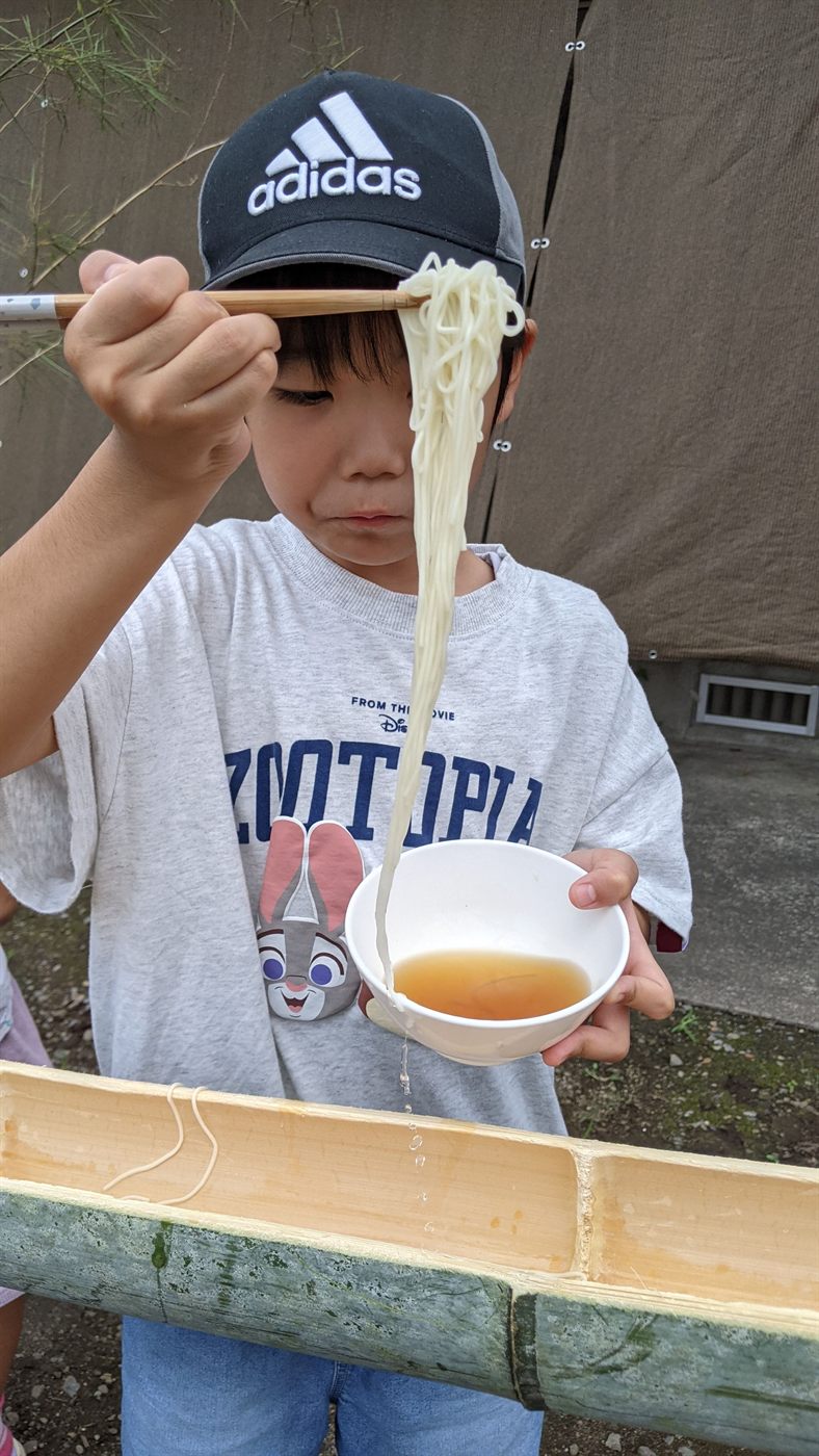 お箸で高く持ち上げた大量のそうめんを見せる男の子