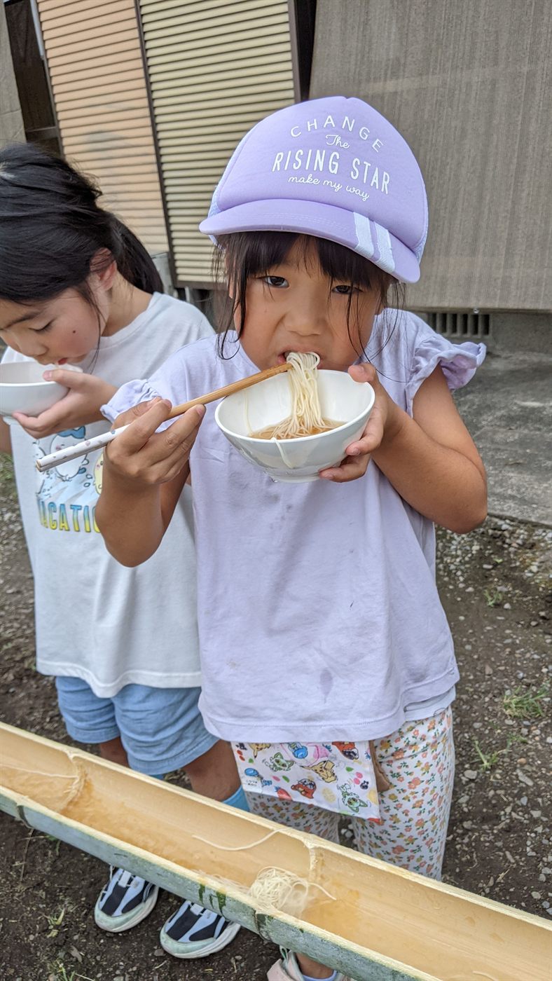 おわんを持ってそうめんをおいしそうに食べる女の子たち