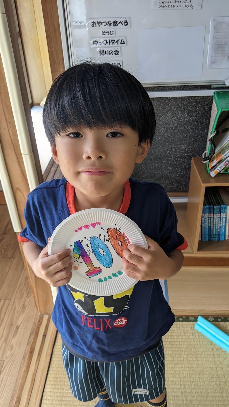 手作りの点数板を手に持って見せる男の子。紙皿にカラフルな数字100が描かれている