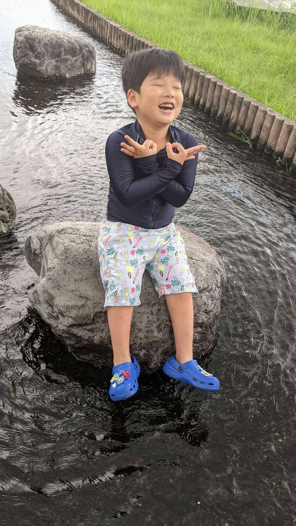 川の中の岩の上で、笑顔でポーズをとる男の子