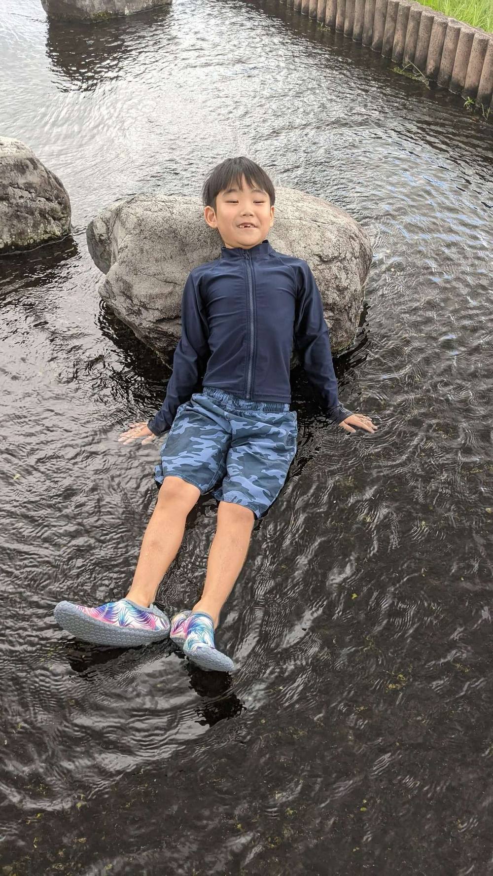 浅い川の中に寝そべって、水に体をひたす男の子