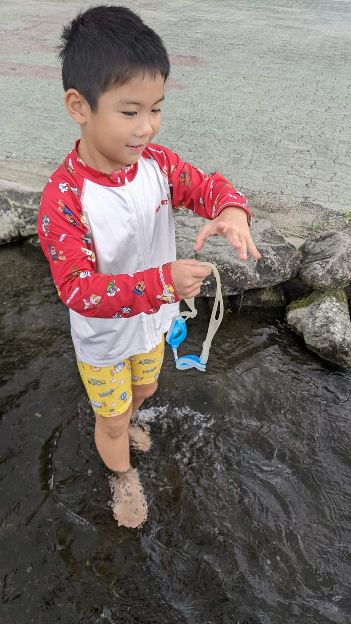 ゴーグルを手に持って、川の中を歩く男の子