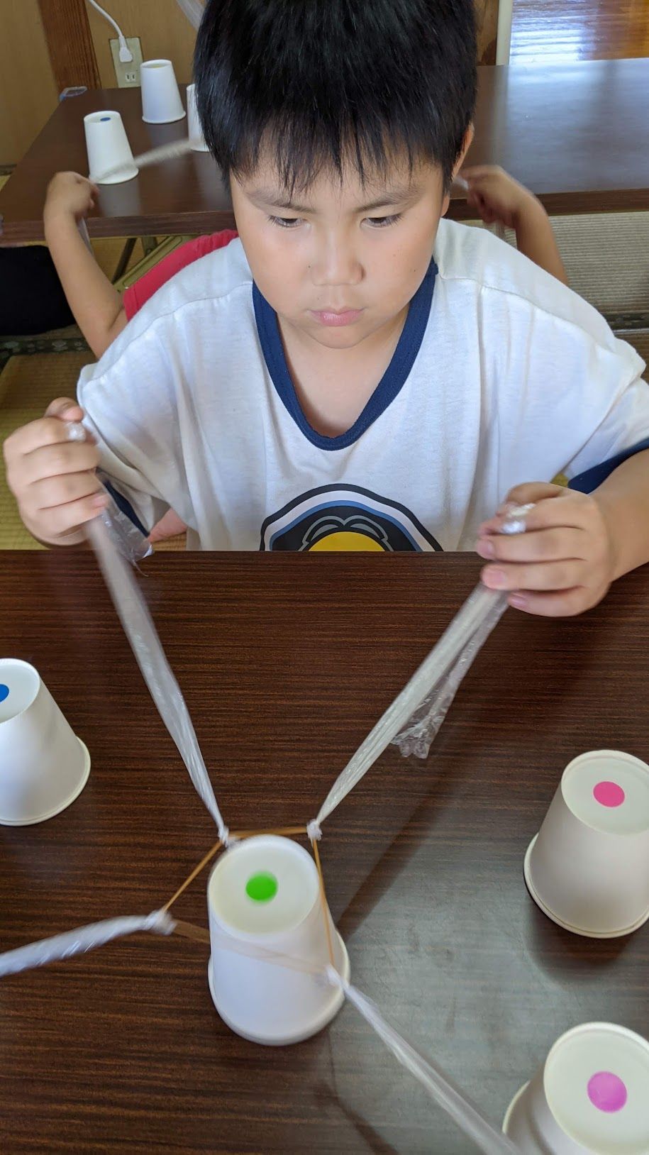 両手でひもを引きながら、紙コップを見つめる男の子