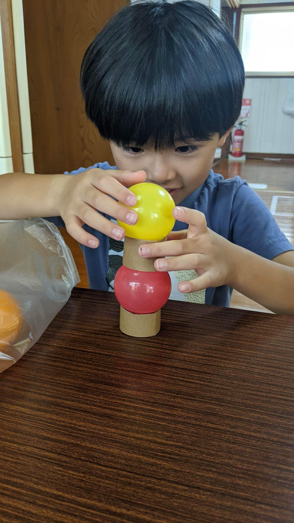 両手で黄色い玉をつまみ、タワーの上にそっと置こうとしている男の子