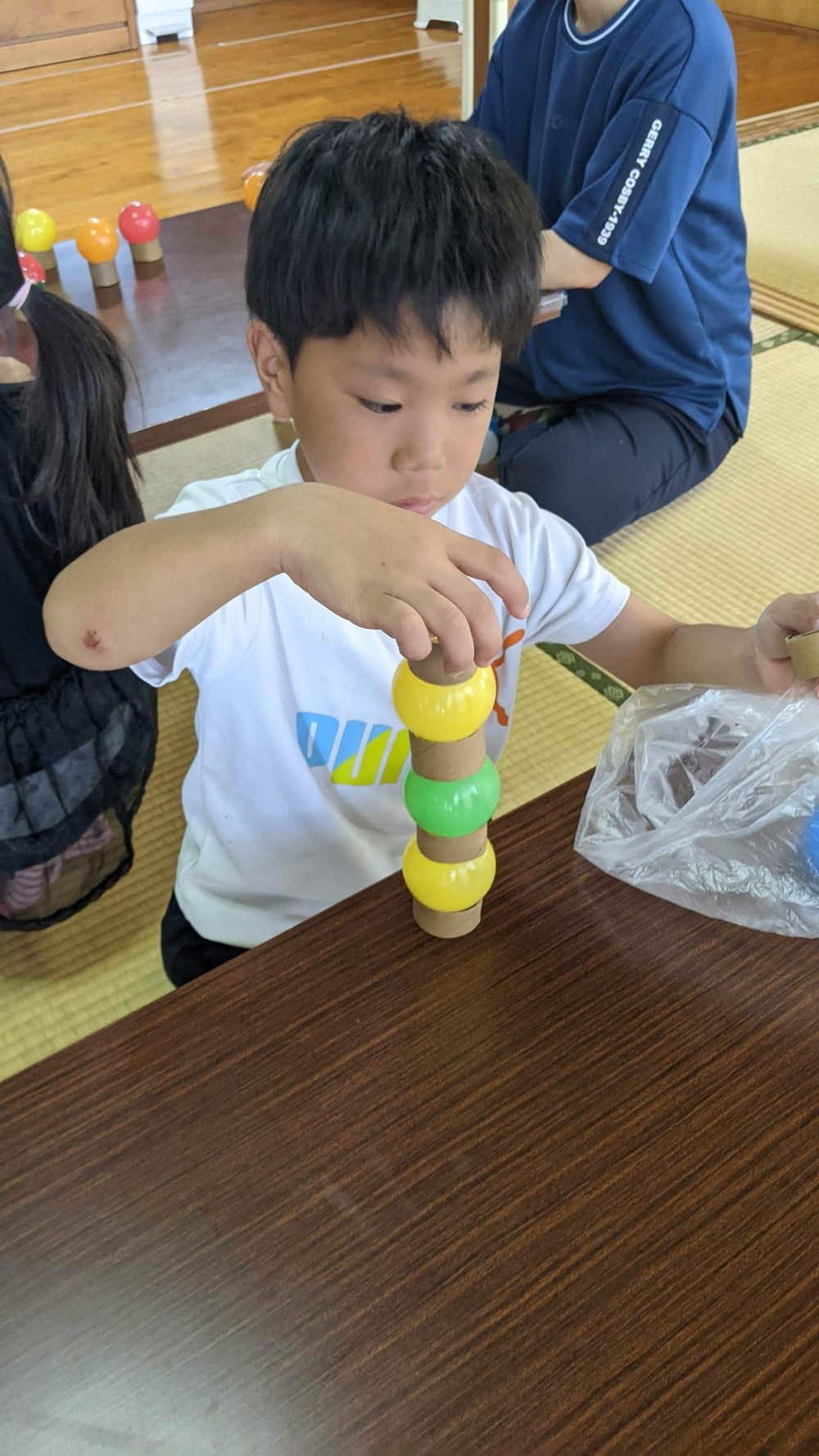 黄色・緑・赤の玉が高く積み上がったタワーに、さらに玉を重ねようとする子ども